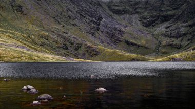Coomloughra Lough etrafındaki engebeli dağları yansıtıyor. Yumuşak dalgalar huzurlu yüzeyi bozar, İrlanda manzarasını.