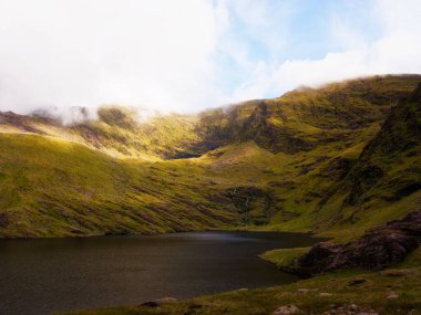 İrlanda 'nın Kerry ilçesinde bulutlu bir gökyüzünün altında canlı yeşil dağlarla çevrili durgun suları gösteren yüksek sesli manzaralar..