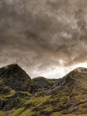 Carrauntoohil, İrlanda 'nın en yüksek dağı, alacakaranlık çökerken dönen bulutlarla çevrilidir. Manzara yeşil tepeler ve kayalık çıkıntılarla dolu..
