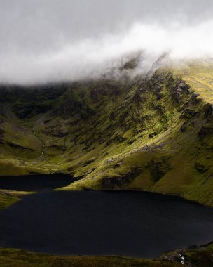 Sivri tepeler, sakin ve karanlık bir gölün üzerindeki girdap gibi sisi delip geçer. Sahne, gizemli ve hayranlık uyandıran doğal güzellikleri yansıtıyor..