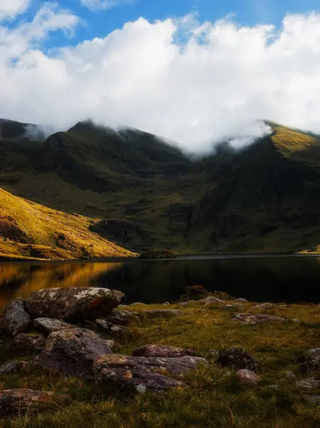 İrlanda 'daki Lough Callee' nin sakin bir öğleden sonra dağları, yansımaları ve kasvetli bulutlarıyla nefes kesici manzarası..