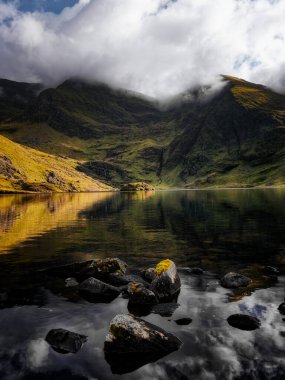 Lough Callee, sakin sularla çarpıcı doğal güzellikler sergiliyor dramatik dağları yansıtıyor. Manzara, bulutlu bir gökyüzünün altında İrlanda 'nın manzaralı sükunetinin özünü yakalıyor..