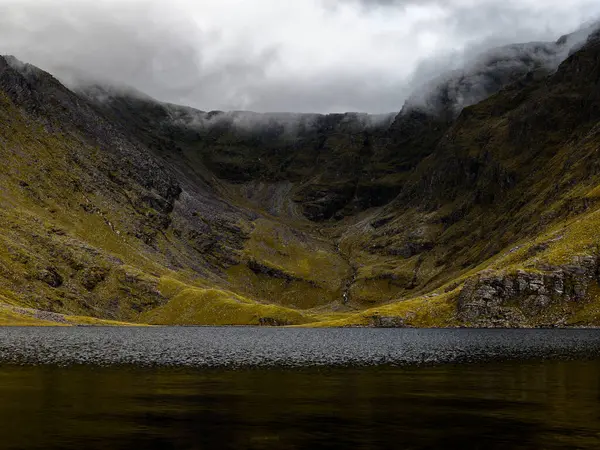 Sakin bir dağ gölü, sis ve yalnızlık hissi uyandıran, heybetli uçurumları yansıtır..