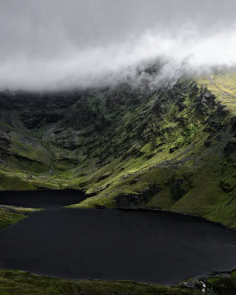 Gizemli bir dağın zirvesi sisle kısmen gizlidir. Yamaçları karanlık ve durgun bir gölle kesişir. Görüntü yalnızlığı ve ihtişamı çağrıştırıyor..