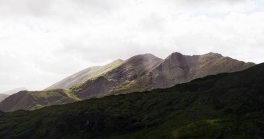Manzara bulutlu günü gösteriyor. Sivri yeşil dağlar sisli gökyüzüne yükselir ve İrlanda 'nın Kerry ilçesinde manzaralı bir manzara yaratır..