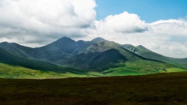 Soluk bir gökyüzünün altındaki kayalık dağ zirveleri ve yuvarlanan tepelerden oluşan nefes kesici bir manzara. Evcilleştirilmemiş manzara.