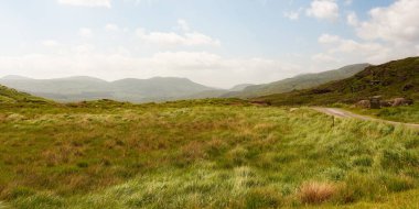 Uçsuz bucaksız otlaklar, ufuktaki yeşil tepelere ve dağlara yol açar. Kerry ilçesi Dunloe geçidinde, düzlüklerden geçen asfalt bir patika sağa gider..
