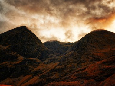 Dramatik dağ siluetleri nefes kesici bir gün batımının altın ışığında yıkanır. Gökyüzü renklerle patlıyor, doğanın sanatının çarpıcı bir görüntüsü..