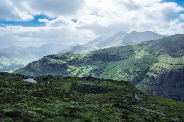 Yuvarlanan yeşil tepeler, uzaktaki sisli dağlara çıkar. Dunloe Geçidi 'nin başından gözlemlenmiştir. İrlanda 'nın Kerry ilçesindeki manzarayı yumuşak ışık kaplıyor.