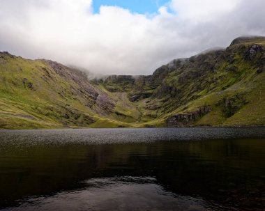 Mistik bir manzara gözler önüne seriliyor, durgun bir göl sisli dağları, vahşiliği ve huzuru yansıtıyor..