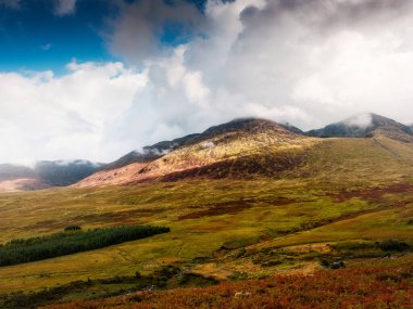 İrlanda 'nın Kerry ilçesindeki dağların ve ovaların manzarası. Zirveler ve vadiler, arka planda ağaçlar ve Carrauntoohill yakınlarında gökyüzünde bulutlar ile görülebilir..