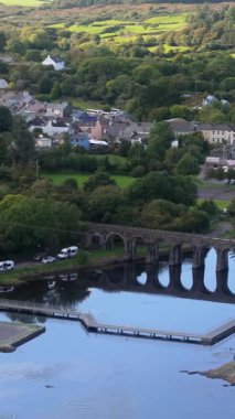 Taştan köprüsü olan nehir manzarası ve alacakaranlıkta deniz kıyısındaki binalar kırsal İrlanda yaşamına bir bakış sağlıyor..