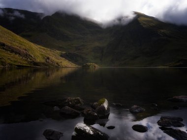 Lough Callee etrafındaki dağları sakin sularda yansıtıyor, alacakaranlık yaklaşırken tepelerin üzerinden yumuşak bulutlar süzülüyor. Bu huzurlu an İrlanda 'nın engebeli güzelliğini yakalıyor..