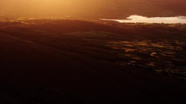 Gün batımında İrlanda kırsalının nefes kesici görüntüsü. Yuvarlanan yeşil tepeler ve sakin bir göl üzerinde altın ışık çağlıyor..