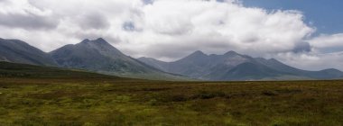 Görkemli dağların gölgesinin altında yemyeşil bir vadi uzanıyor. Huzurlu ve huzurlu bir manzara..