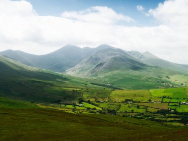 Dağları ve vadiyi görebilirsiniz, hepsi İrlanda 'da. Manzara bulutlu bir gökyüzünün altında yeşil çimlerden, yamaçlardan ve dağlardan oluşur..