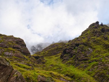 Carrauntoohill geçidi boyunca uzanan manzara engebeli, yeşil bir manzaradır. Bulutlu bir günde, sis ve bulutlar daha yüksek tepeleri kaplıyor, aşağıdaki kayalıkları ve canlı bitkileri öne çıkarıyor..