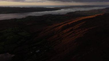 Yukarıdan manzara güzel bir kıyı manzarasını gösteriyor. Dağlar, gün batımında gri bir gökyüzünün altında büyük bir su kütlesine kadar uzanır..