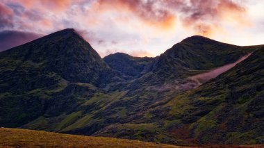 Gün batımında huzurlu bir dağ manzarası. Dağlar parlak, renkli bir gökyüzünün altında dimdik ayakta duruyor. Doğanın güzelliği yakalandı.