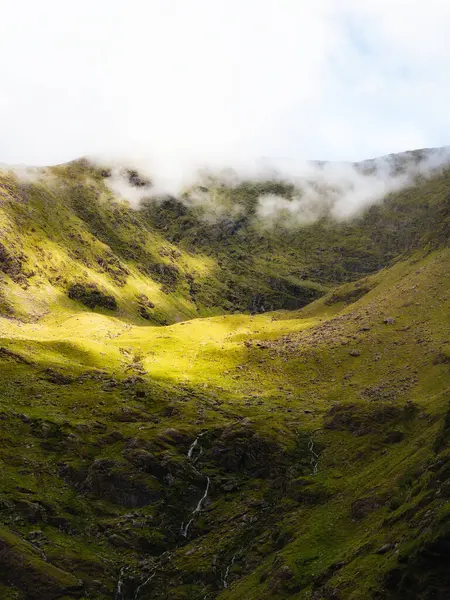 Carrauntoohil 'deki bir vadi yeşil bitki örtüsüyle kaplıdır. Kayaların yüzeyinden dökülen seyrek şelaleler ve Kerry ilçesindeki tepelerin üzerine çöken yoğun bir sis vardır..