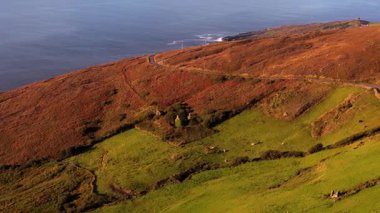 İrlanda 'nın Kerry ilçesindeki Dingle Yarımadası' nda güzel bir manzaranın havadan görüntüsü. Yuvarlanan tepeler, yeşil tarlalar, kıyı yolu, Atlantik Okyanusu ve eski bir taş harabe görülebilir..