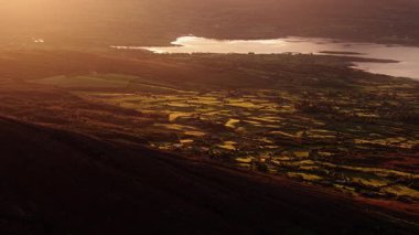 Büyüleyici bir günbatımı İrlanda kırsalını aydınlatır. Altın ışığın dalgalı tepelere ve huzurlu göle vuruşunu izleyin..