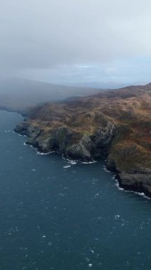 İrlanda kıyıları havadan alındı. Gri, bulutlu bir günde koyu mavi okyanus suyuyla kayalık bir sahil şeridi gösteriyor..