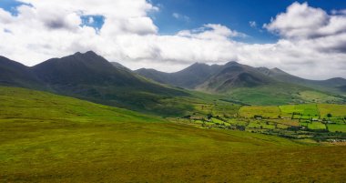 Canlı yeşil yamaçların yumuşak yamaçları, doğanın gücü ve güzelliğinin bir kanıtı olan, yükselen zirvelere önderlik eder..