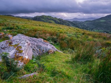 Coomloughra At Nalı 'nın manzarası bulutlu bir günde İrlanda' nın Kerry ilçesinde yeşil tepeler ve bulutlu gökyüzüyle.