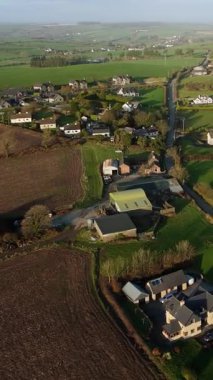 Bu İrlanda 'daki kırsal bir bölgenin kuş bakışı görüntüsü. Çiftlik evleri, parlak yeşil tarlalar ve akşam erken saatlerde arazide dolanan dar bir yol gösteriyor..