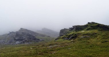 Çim ve çalılıklarla kaplı Rocky dağları neredeyse tamamen kalın sisle kaplıdır. Düşük görüş mesafesi İrlanda manzarasında bulutlu ve bulutlu bir gün olduğunu gösteriyor..