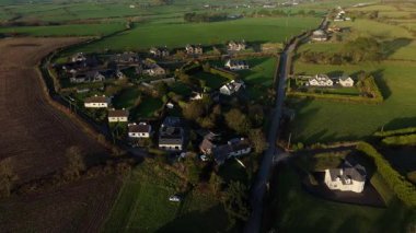Alacakaranlıktaki İrlanda kırsalının hava manzarası yeşil tarlalara, çiftliklere, evlere ve dolambaçlı bir yola bakıyor..