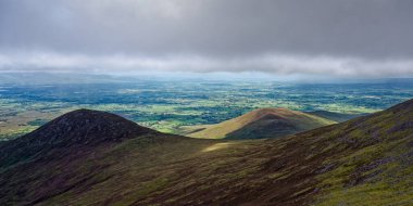 İrlanda kırsal manzarası, yuvarlanan tepeler ve yeşil vadiler, Coomloughra At nalı üzerinden görüldüğü gibi, arka planda bulutlu bir gökyüzü ile.