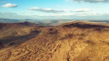 İrlanda, County Cork 'taki Priest' s Leap çevresindeki dağlık araziye manzaralı bir bakış. Ufukta rüzgar türbinleri görülebiliyor ve doğal manzaraya karşı uzak bir kontrastı sağlıyor..