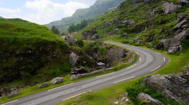 Sarmal bir yol İrlanda 'daki Dunloe' nin pitoresk geçidini kesiyor. Dar asfalt yolu çevreleyen yeşil yamaçlar ve kayalık arazi parçalı bulutlu bir günde.