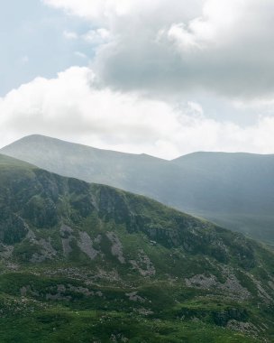 Manzaralı bir manzara İrlanda 'nın Dunloe bölgesindeki engebeli yeşil dağları yakalar. Bulutlar gökyüzünü dolduruyor, resim gibi bir manzara yaratıyor..