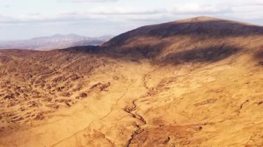 Majestic Highlands 'da. Parçalı bulutlu bir gökyüzü altında engebeli dağların ve uzak rüzgar türbinlerinin nefes kesici hava manzarası..