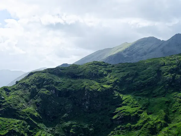 Dağların manzarası, manzara ve yeşil yosunlarla kaplı tepeler. Dunloe Geçidi, parçalı bulutlu bir günde İrlanda 'nın Kerry ilçesinde bulunan dar bir dağ geçididir..