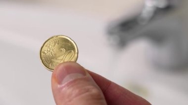 Elde para, banyoda musluk ve akan su. Seçici odaklanma. Tüketim ve doğal kaynakların korunması, ev bütçesi parası