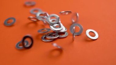 Bir grup galvanize metal yıkayıcı ağır çekimde turuncu renkli arka plan üzerine düşüyor. Çelik galvanizli uzay araçları bağlanmak için. Mühendislik konsepti. Makro. Döndürme