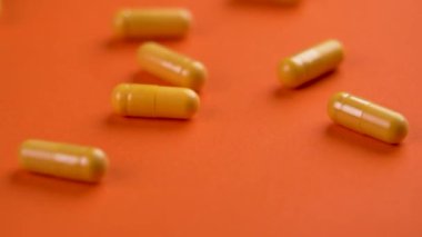 Renkli sarı ilaç kapsülleri parlak turuncu yaratıcı arka plana düşüyor. Makro. Yavaş çekim
