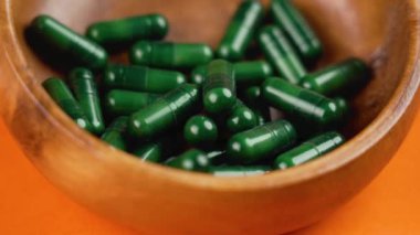 Alternatif diyet bitkisel ilaçların yeşil takviye kapsülleri parlak turuncu arka planda ahşap kasede. Döndürme