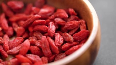 A hand takes a handful of red dried ripe goji berries from a wooden bowl. Organic wolfberry close up. Rotation. Slow motion. Superfood ingredient