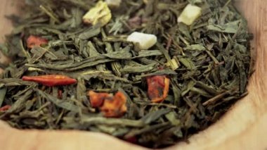 Chinese green tea leaves with dried fruit pieces in a rustic wooden bowl. Healthy drink. Macro. Rotation