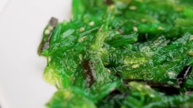Green Japanese seaweed salad in white kitchen plate. Macro. Rotation
