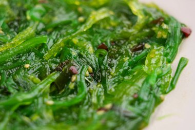 Green Japanese seaweed salad in white kitchen plate. Macro