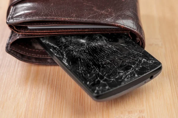 A broken cellphone with a crushed shattered glass black screen in a brown leather wallet. Conceptual view