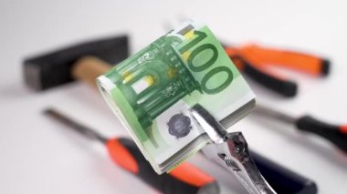 Cash european money clamped in a metal wrench with industrial repair tools in blur. Conceptual view