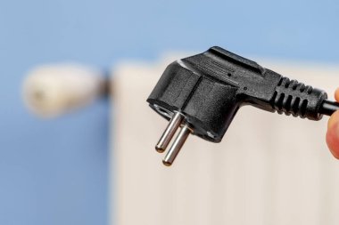 Electrical plug in hand with disconnected home heating radiator. Energy saving concept