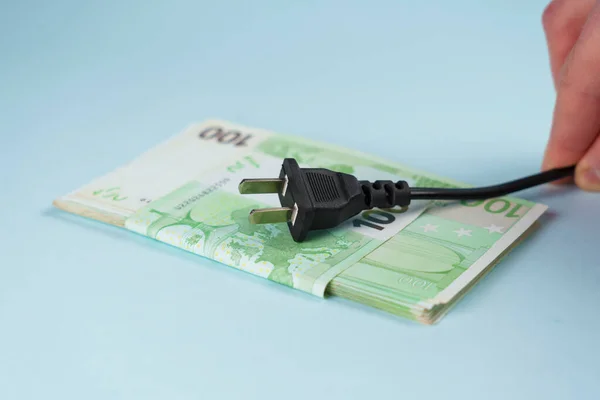 Power plug in hand on euro money background. Expensive electricity supply concept